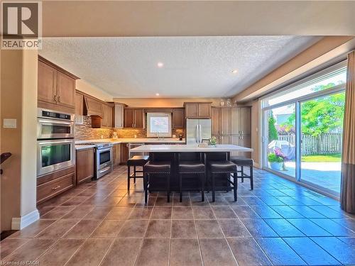Spacious open-concept kitchen and dining area featuring wood-finish cabinetry, stainless steel appliances, tile flooring throughout, a large center island with seating, and expansive glass sliding doo - 913 Valebrook Court, Kitchener, ON - Indoor Photo Showing Kitchen