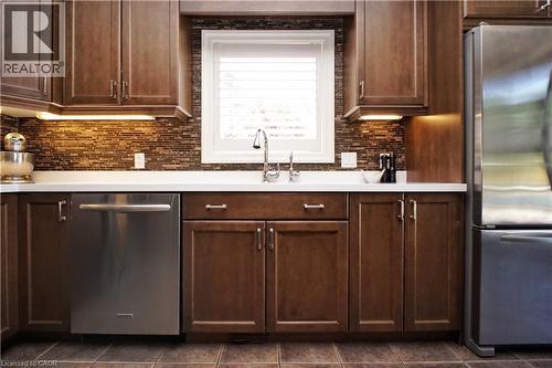 Full-height cabinetry with under-cabinet lighting, mosaic tile backsplash, stainless steel appliances, and a window with blinds - 913 Valebrook Court, Kitchener, ON - Indoor Photo Showing Kitchen