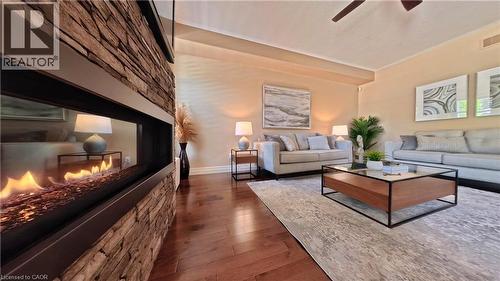 Sophisticated living room showcasing a linear fireplace with stacked stone surround, rich wood-finish flooring, and recessed ceiling lighting - 913 Valebrook Court, Kitchener, ON - Indoor Photo Showing Living Room With Fireplace