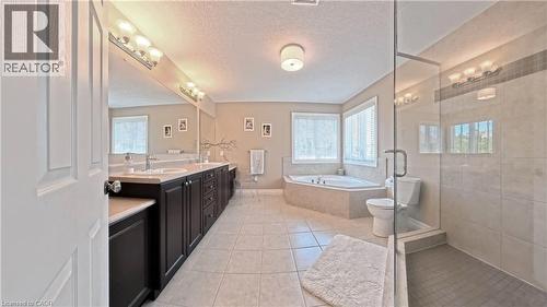 Double vanity with undermount sinks, built-in soaking tub, walk-in shower with glass enclosure, tiled flooring, and multiple windows with blinds - 913 Valebrook Court, Kitchener, ON - Indoor Photo Showing Bathroom