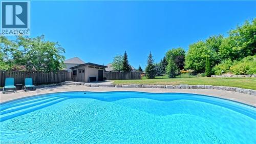 In-ground swimming pool with integrated steps, surrounded by a paved deck, retaining wall, and a wood privacy fence - 913 Valebrook Court, Kitchener, ON - Outdoor With In Ground Pool With Backyard