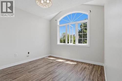 Bright, light-filled room featuring a striking arched transom window with grid detailing and white frame, gleaming wood-finish flooring, and a contemporary pendant light fixture overhead - 43 Decaro Crescent, Cambridge, ON - Indoor Photo Showing Other Room