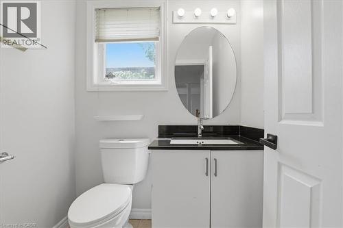 Modern bathroom featuring a sleek oval mirror with integrated lighting, black quartz countertop, white cabinetry with chrome hardware, ceramic vessel sink with chrome faucet, and a white ceramic toile - 43 Decaro Crescent, Cambridge, ON - Indoor