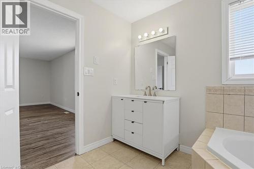 Spa-inspired primary bathroom featuring a white vanity with multiple drawers and brushed nickel hardware, a framed mirror with integrated lighting, tile surround accents, and a soaking tub - 43 Decaro Crescent, Cambridge, ON - Indoor Photo Showing Bathroom