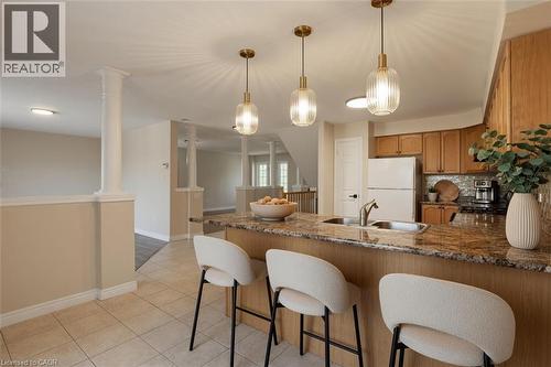 Open-concept kitchen and dining area featuring a wood-finish island with waterfall edge, granite countertop, three pendant lights with brass fixtures, white upholstered seating, tile flooring, and sta - 43 Decaro Crescent, Cambridge, ON - Indoor