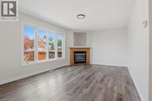 Spacious living area featuring engineered wood-finish flooring throughout, abundant natural light from multi-panel glass doors opening to an outdoor deck, and a corner fireplace with wood mantel surro - 43 Decaro Crescent, Cambridge, ON - Indoor Photo Showing Living Room With Fireplace