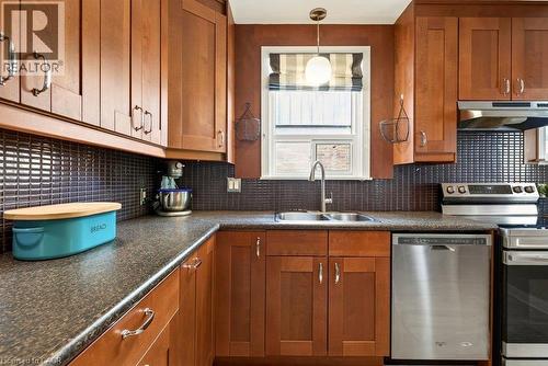 Warm wood cabinetry with brushed metal hardware anchors this kitchen, featuring stainless steel appliances, a subway tile backsplash, and a natural light-filled window above the sink - 23 Kipling Road, Hamilton, ON - Indoor Photo Showing Kitchen With Stainless Steel Kitchen With Double Sink
