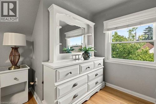 Bright secondary bedroom featuring a white dresser with mirror and multiple drawers, hardwood flooring, large windows with natural light, and gray wall finishes - 23 Kipling Road, Hamilton, ON - Indoor