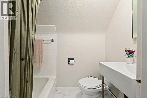 Clean, bright bathroom featuring a white ceramic vessel sink with a contemporary wall-mounted faucet, white subway tile surround, porcelain flooring, an enclosed shower/tub combination with a neutral - 23 Kipling Road, Hamilton, ON - Indoor Photo Showing Bathroom
