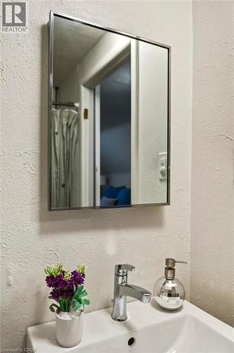 Modern bathroom vanity featuring a sleek chrome faucet, white ceramic sink with integrated countertop, polished metal-framed medicine cabinet with mirrored doors, and neutral textured wall finishes - 23 Kipling Road, Hamilton, ON - Indoor Photo Showing Bathroom