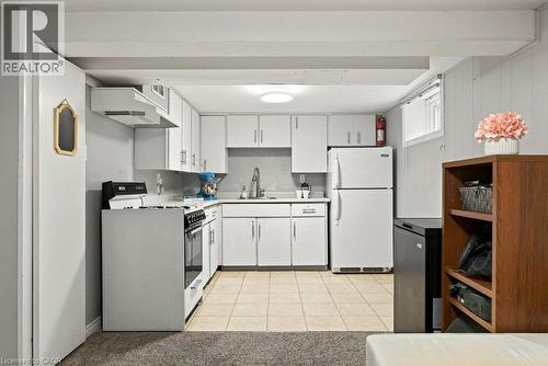 Galley kitchen featuring white cabinetry, stainless steel appliances including a gas range and refrigerator, tile flooring, and ample counter and storage space - 23 Kipling Road, Hamilton, ON - Indoor Photo Showing Kitchen