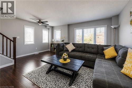 Spacious living area featuring wood-finish flooring, multiple windows with blinds, a ceiling fan, and a wood staircase with dark balusters - 750 Lawrence Street Unit# 86, Cambridge, ON - Indoor Photo Showing Living Room