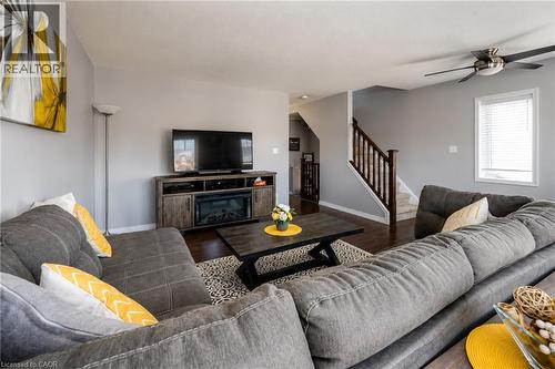 Hardwood-finish flooring, built-in media console with electric fireplace, ceiling fan with integrated lighting, and a staircase with wood railings - 750 Lawrence Street Unit# 86, Cambridge, ON - Indoor Photo Showing Living Room
