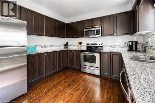 Dark wood cabinetry complemented by light-toned countertops, stainless steel appliances, a subway tile backsplash, and wood-finish flooring - 750 Lawrence Street Unit# 86, Cambridge, ON - Indoor Photo Showing Kitchen With Double Sink With Upgraded Kitchen