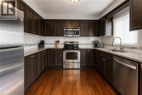U-shaped kitchen with dark wood-finish cabinetry, granite countertops, and stainless steel appliances - 750 Lawrence Street Unit# 86, Cambridge, ON - Indoor Photo Showing Kitchen With Double Sink