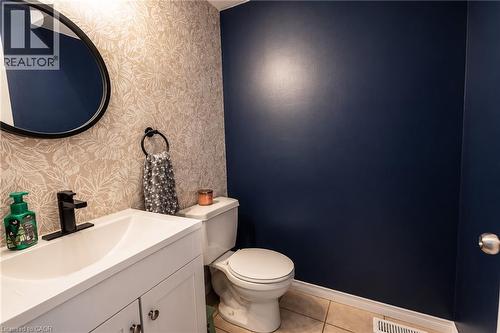 Powder room with a white vanity, black faucet, circular mirror, and patterned wallpaper accent wall - 750 Lawrence Street Unit# 86, Cambridge, ON - Indoor Photo Showing Bathroom
