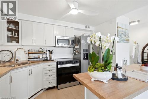Kitchen featuring white cabinetry, stainless steel appliances, a ceiling fan with integrated lighting, and a breakfast bar with a wood-finish countertop - 8 Woodman Drive S Unit# 708, Hamilton, ON - Indoor Photo Showing Kitchen With Double Sink