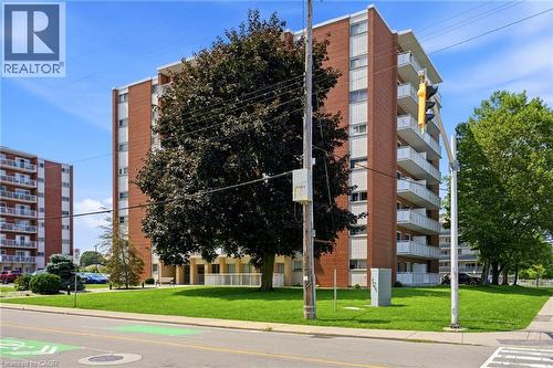 Brick facade building with multiple balconies, a manicured lawn, and mature trees - 8 Woodman Drive S Unit# 708, Hamilton, ON - Outdoor With Balcony With Facade