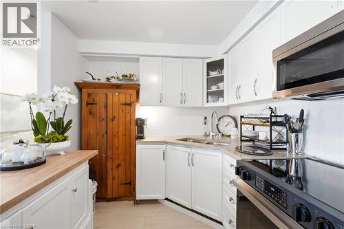White cabinetry, stainless steel microwave, integrated cooktop, corner sink, and a built-in wooden cabinet - 8 Woodman Drive S Unit# 708, Hamilton, ON - Indoor Photo Showing Kitchen With Double Sink