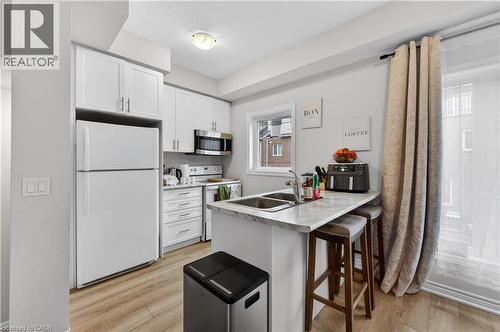 Modern kitchen featuring white cabinetry, stainless steel microwave, light-toned wood-finish flooring, and a double-basin sink - 19 Picardy Drive Unit# 13, Hamilton, ON - Indoor Photo Showing Kitchen With Double Sink