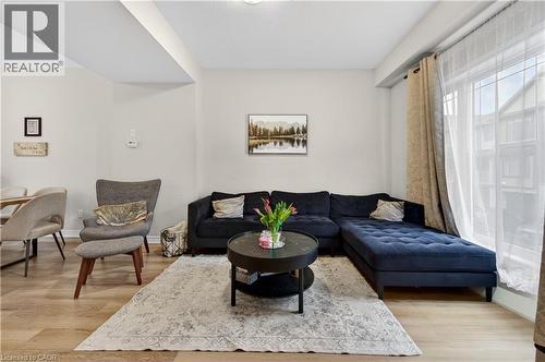 Living area featuring light-toned walls, wood-finish flooring, and a large window - 19 Picardy Drive Unit# 13, Hamilton, ON - Indoor Photo Showing Living Room