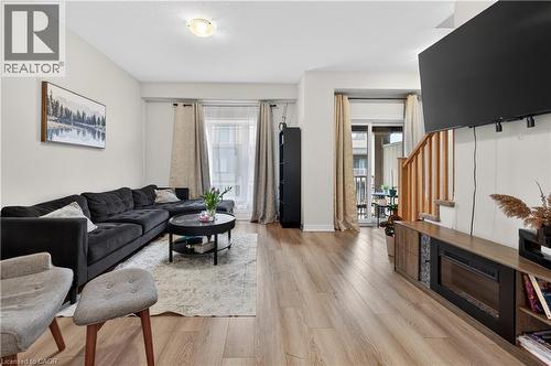 Open-concept living area featuring wood-finish flooring, a built-in electric fireplace, and a sliding glass door leading to a balcony - 19 Picardy Drive Unit# 13, Hamilton, ON - Indoor Photo Showing Living Room With Fireplace
