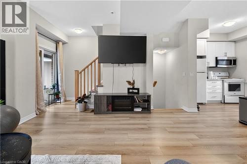Open-concept living area with wood-finish flooring, a contemporary staircase with wood railings, and a kitchen featuring white cabinetry and stainless steel appliances - 19 Picardy Drive Unit# 13, Hamilton, ON - Indoor