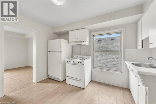 Kitchen featuring white cabinetry, wood-finish flooring, a white gas range, a white refrigerator, and a stainless steel sink - 1367 Cannon Street E, Hamilton, ON - Indoor Photo Showing Kitchen