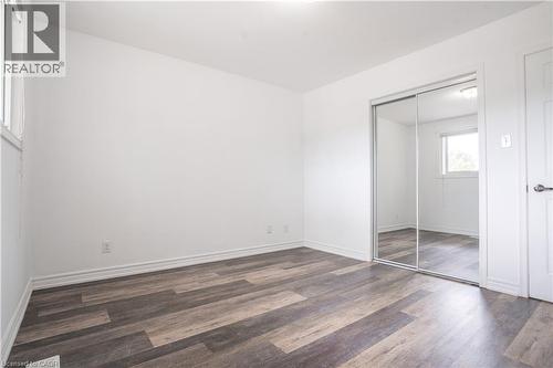 Spacious bedroom featuring rich wood-finish flooring, mirrored sliding closet doors, abundant natural light from windows, white painted walls, and clean architectural lines throughout - 695 Glen Forrest Boulevard Unit# Upper, Waterloo, ON - Indoor Photo Showing Other Room