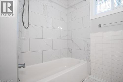 Spa-inspired bathroom featuring large-format marble-look tile walls, a deep soaking bathtub with chrome fixtures, a frameless glass shower enclosure, and natural light from a transom window - 695 Glen Forrest Boulevard Unit# Upper, Waterloo, ON - Indoor Photo Showing Bathroom
