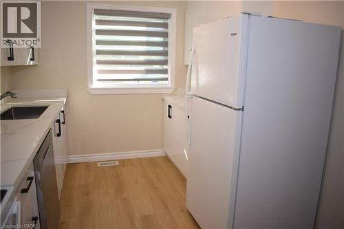 White cabinetry with dark hardware, a stainless steel sink, light-toned wood-finish flooring, a white refrigerator, and a window with blinds - 655 Albert Street Unit# A, Waterloo, ON - Indoor Photo Showing Kitchen