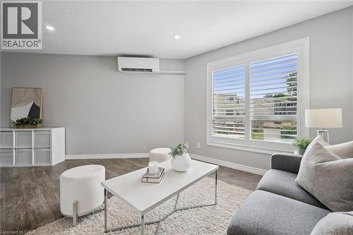 Recessed ceiling lighting, wood-finish flooring, wall-mounted air conditioning unit, window with plantation shutters, and light gray wall paint - 60 Elmsdale Drive Unit# 25, Kitchener, ON - Indoor Photo Showing Living Room