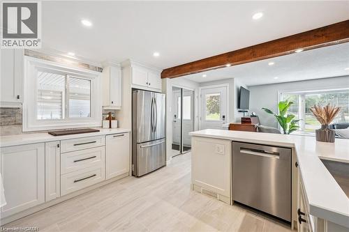 White cabinetry with dark hardware, stainless steel appliances, light-toned tile flooring, recessed lighting, and a wood beam accent - 659 Glen Forrest Boulevard, Waterloo, ON - Indoor Photo Showing Kitchen With Stainless Steel Kitchen