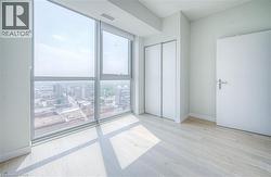 Floor-to-ceiling windows, light wood-finish flooring, white walls, double sliding closet doors, and a paneled white door with a lever handle - 