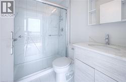 Glass-enclosed shower with white tiled walls, light wood-finish vanity with an integrated sink, and a mirrored medicine cabinet - 