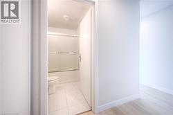 Bathroom featuring a white toilet, tile flooring, and a shower-over-tub with frosted glass sliding doors - 