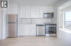 Modern kitchen with white upper cabinetry, stainless steel appliances, wood-finish flooring, and light-toned countertops - 
