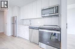 Contemporary kitchen featuring light wood-finish flooring, white flat-panel cabinetry, stainless steel appliances, and a tiled backsplash - 