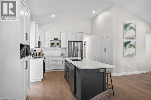 Modern kitchen featuring white cabinetry with brushed metal hardware, stainless steel appliances including a refrigerator and range hood, quartz countertops, a contrasting black kitchen island with se - 1041 Shepherd'S Drive, Burlington, ON - Indoor Photo Showing Kitchen With Upgraded Kitchen