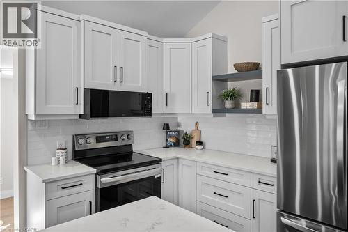 Modern kitchen featuring white shaker-style cabinetry with black hardware, stainless steel appliances including a slide-in range and refrigerator, white subway tile backsplash, and light-filled counte - 1041 Shepherd'S Drive, Burlington, ON - Indoor Photo Showing Kitchen With Upgraded Kitchen
