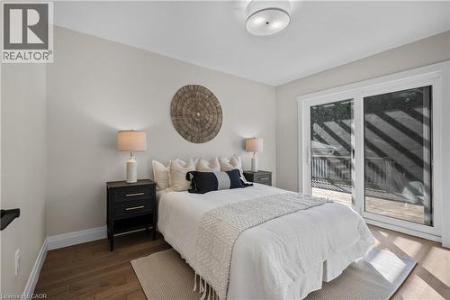 Bright primary bedroom featuring wood-finish flooring, a queen-size bed with upholstered headboard, dual nightstands with integrated lighting, and sliding glass doors opening to a private balcony with - 1041 Shepherd'S Drive, Burlington, ON - Indoor Photo Showing Bedroom