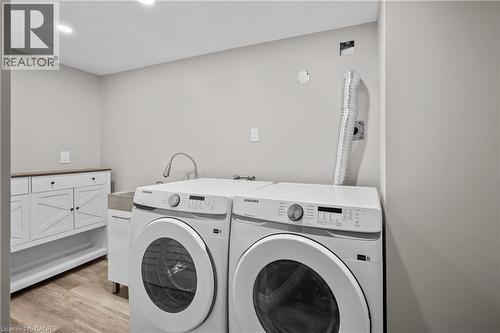 Laundry area featuring wood-finish flooring, recessed lighting, white cabinetry with dark hardware, and a utility sink with a gooseneck faucet - 1041 Shepherd'S Drive, Burlington, ON - Indoor Photo Showing Laundry Room