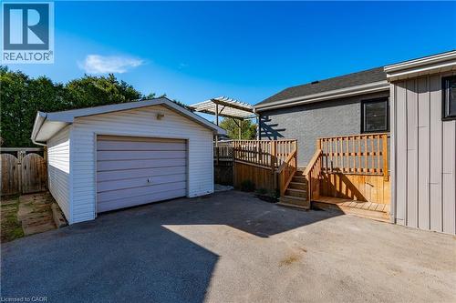 Spacious backyard featuring a detached single-car garage with paneled doors, wooden deck with railings, mature landscaping, and concrete driveway parking area - 1041 Shepherd'S Drive, Burlington, ON - Outdoor With Exterior