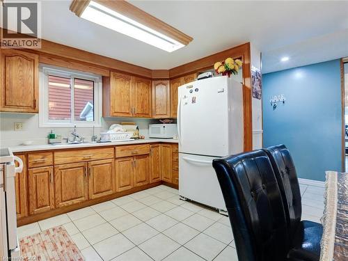 Kitchen featuring wood cabinetry, white countertops, a stainless steel sink, and white tile flooring - 128 Macatee Place, Cambridge, ON - Indoor Photo Showing Kitchen