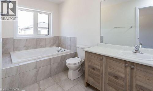 Built-in soaking tub, large window, wood-finish vanity, integrated sink, and tiled flooring - 16 Monteith Drive, Brantford, ON - Indoor Photo Showing Bathroom