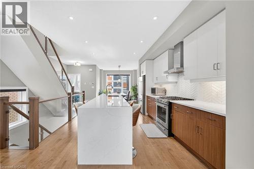 Open-concept kitchen featuring an oversized island with a solid surface countertop, white upper cabinetry, wood-finish lower cabinetry, and stainless steel appliances - 60 Arkell Road Unit# 57, Guelph, ON - Indoor Photo Showing Kitchen With Upgraded Kitchen