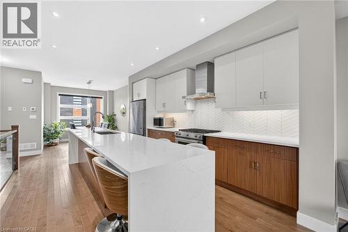 Kitchen featuring a waterfall island, stainless steel appliances, wood-finish flooring, white upper cabinetry, and contrasting wood-finish lower cabinetry - 60 Arkell Road Unit# 57, Guelph, ON - Indoor Photo Showing Kitchen With Upgraded Kitchen
