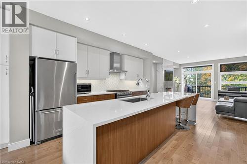 Kitchen featuring a large waterfall island, stainless steel appliances, white cabinetry, wood-finish flooring, and a chevron tile backsplash - 60 Arkell Road Unit# 57, Guelph, ON - Indoor Photo Showing Kitchen With Stainless Steel Kitchen With Upgraded Kitchen