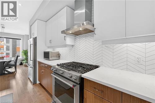 Kitchen featuring white cabinetry, wood-finish lower cabinetry, white countertops, stainless steel appliances, and a herringbone-patterned tile backsplash - 60 Arkell Road Unit# 57, Guelph, ON - Indoor Photo Showing Kitchen With Stainless Steel Kitchen With Upgraded Kitchen