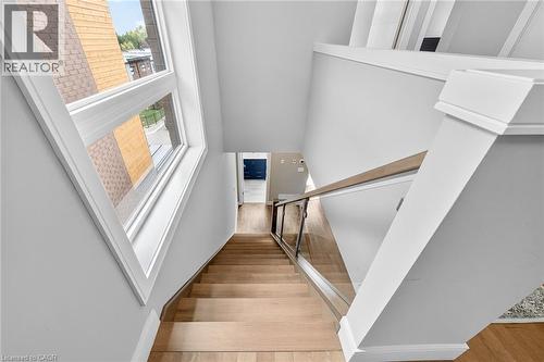 Hardwood stairs with a glass and wood-finish railing, complemented by white trim and a prominent window - 60 Arkell Road Unit# 57, Guelph, ON - Indoor Photo Showing Other Room
